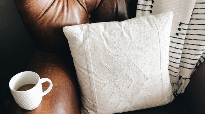 Sofa mit Kissen und einer Kaffeetasse auf der Lehne | © Unsplash / Stephanie Harvey