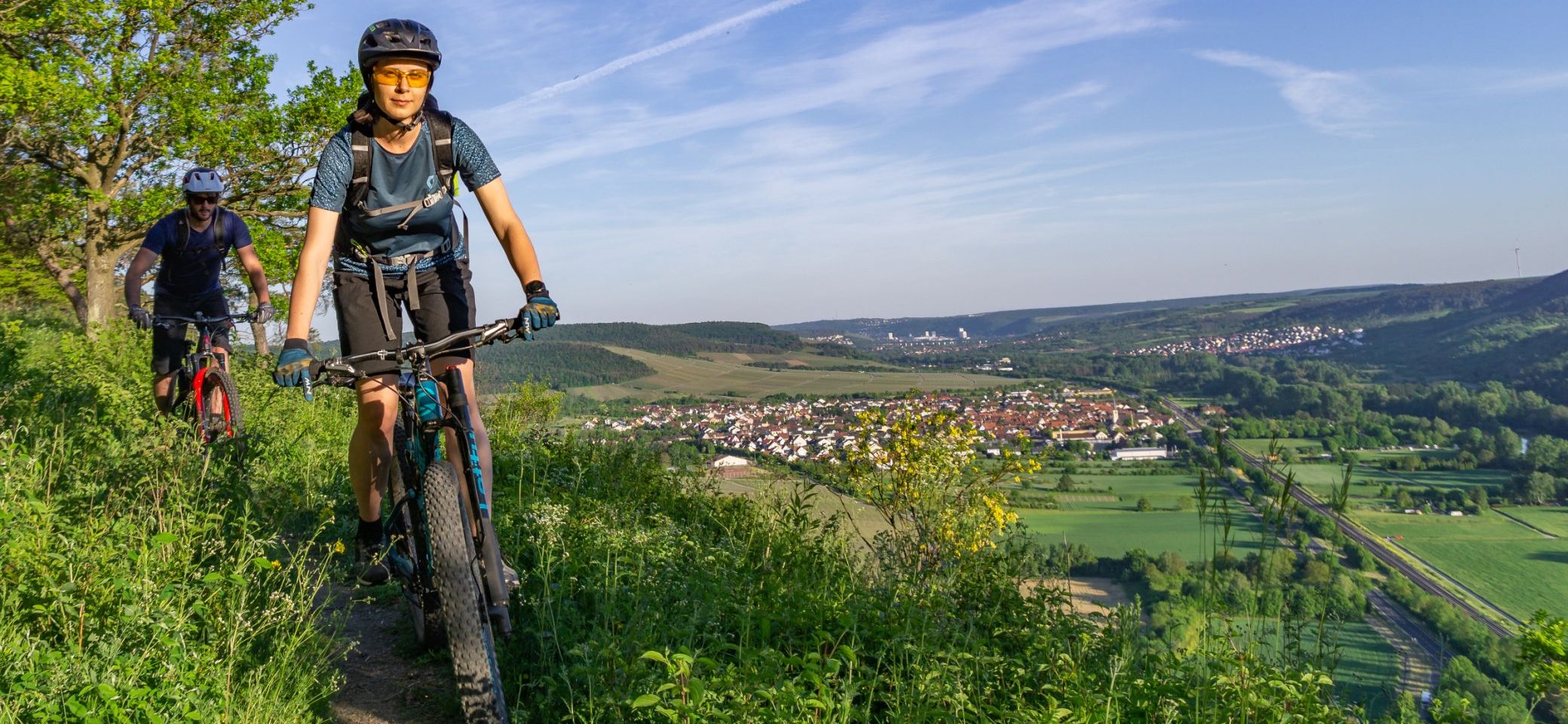 Schöne Landschaft, links am Bildrand sind zwei Mountainbiker, die einen Trail hinunterfahren | © DAV Wuerzburg