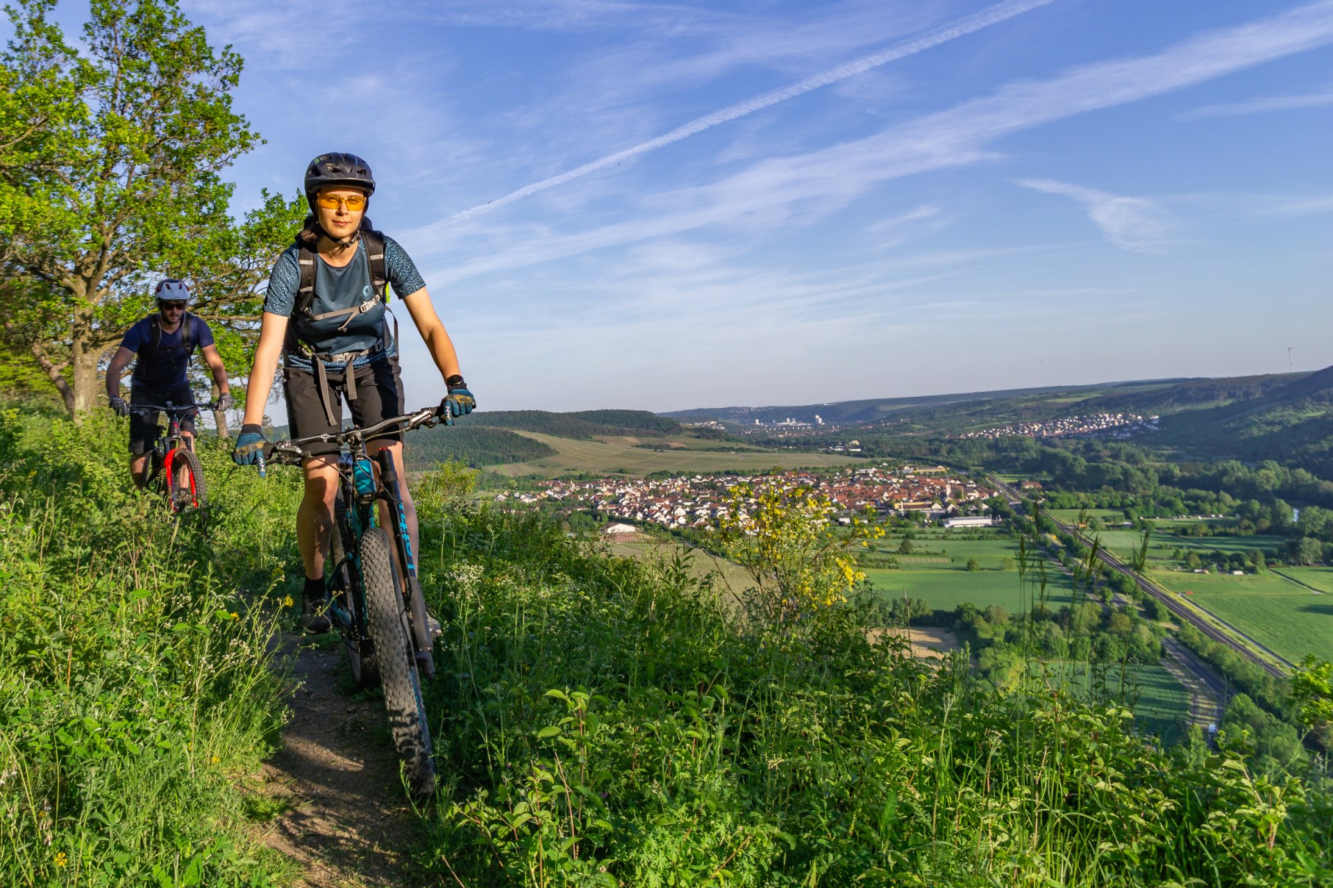Schöne Landschaft, links am Bildrand sind zwei Mountainbiker, die einen Trail hinunterfahren | © DAV Wuerzburg